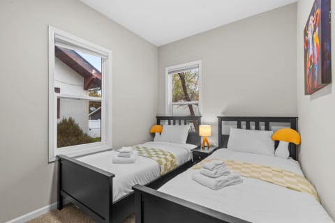 A well-lit bedroom with two twin beds, colorful decor, and a warm bedside lamp.