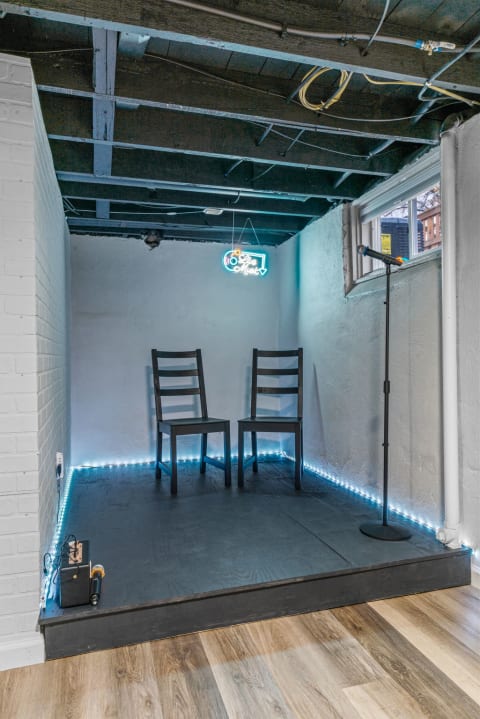 Cozy basement performance space with two black chairs and a neon 'Live Music' sign.