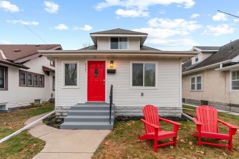 Single-family house with a red door and red chairs in the front yard.
