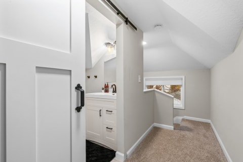 View of a modern attic with a bathroom through a sliding barn door and a carpeted hallway.