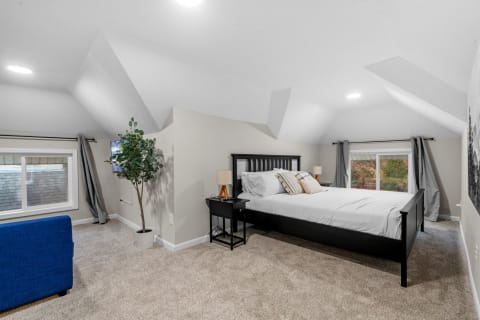 Cozy attic bedroom featuring a bed, blue sofa, and potted plant under a sloped ceiling.
