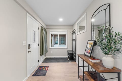 Entryway featuring a white door, green curtains, a coat rack, and a wooden console table with decorations.