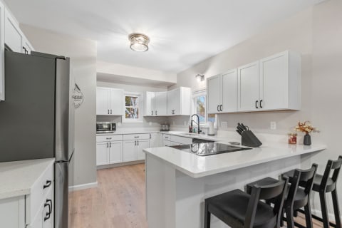 Contemporary kitchen featuring white cabinetry, quartz countertops, and black bar stools.