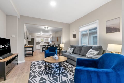 A modern living room with blue armchairs, a gray sofa, and an open kitchen design.