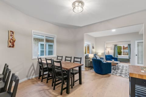 Dining area with a wooden table and black chairs leading to a living room with blue chairs and natural light.