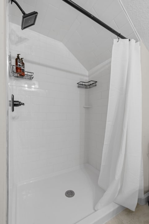 A modern shower interior with white tiles and a black showerhead.