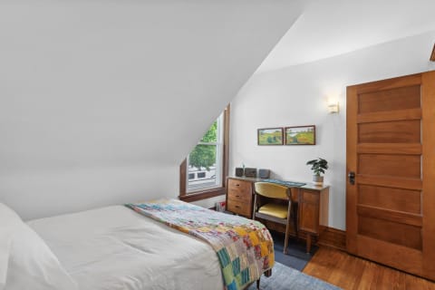 A cozy bedroom featuring a bed with a colorful quilt, a desk, and a window view.