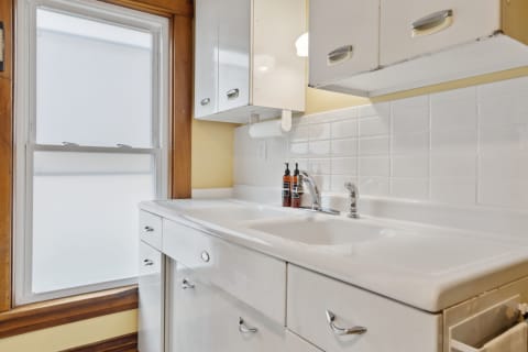 Modern kitchen sink with white cabinets and frosted window.