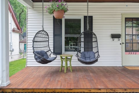 Two hanging wicker chairs with gray cushions on a wooden porch.