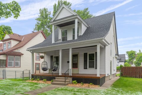 Exterior of a two-story house featuring a porch with hanging chairs and a green lawn.