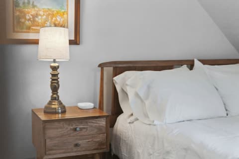 A wooden bed with white linens and a nightstand with a lamp in a cozy bedroom.