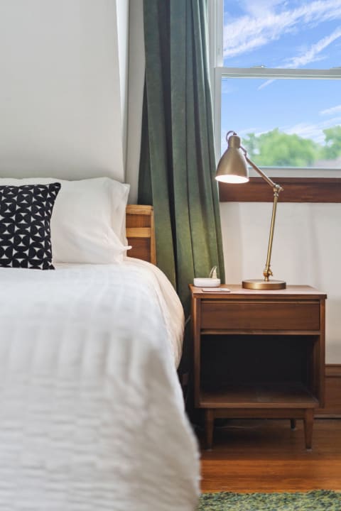 A serene bedroom with a neatly made bed, a decorative pillow, and a stylish nightstand with a desk lamp.