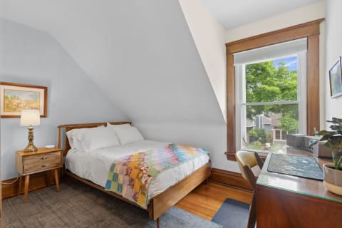 A cozy bedroom with a sloped ceiling, a bed with a colorful quilt, and a desk by the window.
