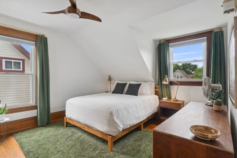 A bright and cozy bedroom featuring a white bed, green curtains, and wooden furniture.