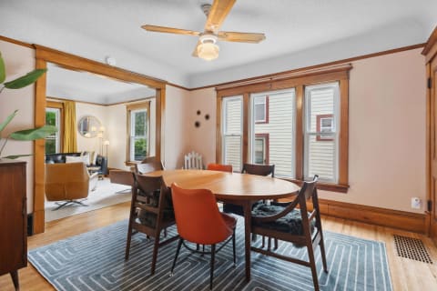A stylish dining area with a wooden table and varied seating, leading into a living room with a leather sofa.