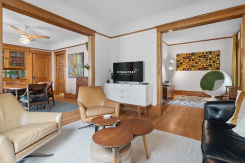 Modern living room with tan leather chairs, white cabinet, and vibrant artwork.
