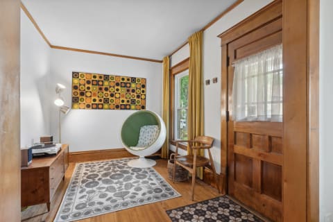 A cozy room corner with an egg-shaped chair, wooden cabinet, and colorful wall art.