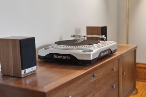 Numark turntable on a wooden cabinet with speakers on either side.