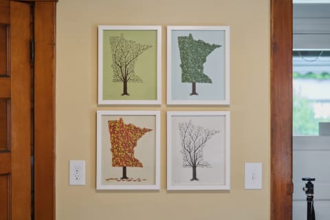 Four framed illustrations of trees with seasonal variations hanging on a wall.