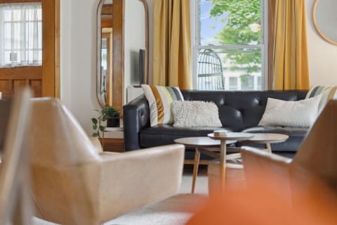 A cozy living room featuring a black leather sofa, decorative pillows, and natural light from a window.