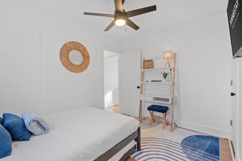 Bright and modern bedroom with a plush bed, decorative mirror, and dedicated workspace.