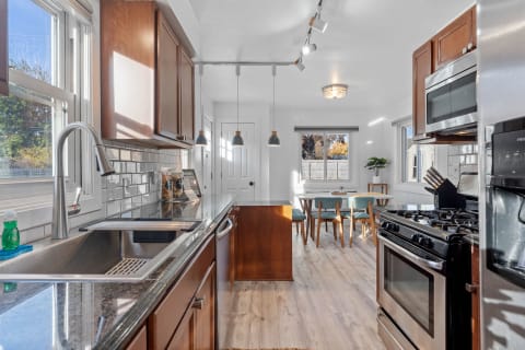 A modern kitchen featuring granite countertops, wood cabinets, and a dining space with mid-century chairs.
