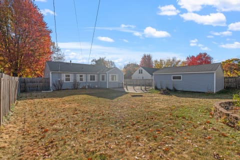 Single-story blue home with a spacious yard and autumn leaves scattered on the grass.