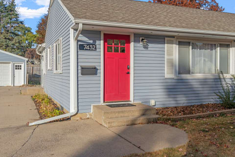 Entrance of a home with a red door, blue siding, and well-maintained surroundings.