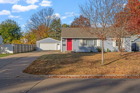 A single-story house with a red door and autumn foliage in the yard.