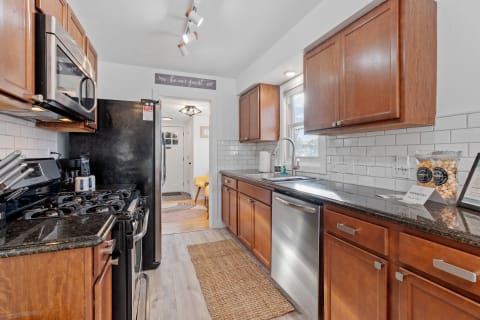A modern kitchen featuring wooden cabinets, granite countertops, and stainless steel appliances, with a sign that says 'be our guest.'