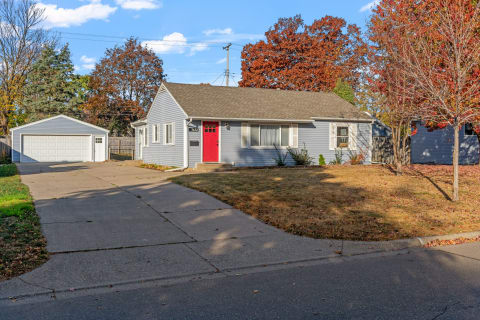Ranch-style home with red door and autumn trees in a residential neighborhood.