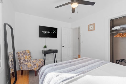 Modern bedroom with a bed, ceiling fan, TV, and decorative chair.