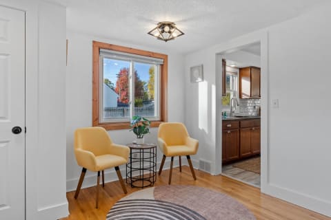 A cozy reading area with yellow chairs and a view of autumn trees outside the window, adjacent to a modern kitchen.