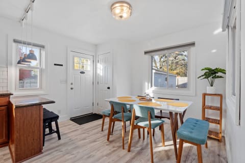 Bright dining area with teal chairs and a white table under natural light from windows.