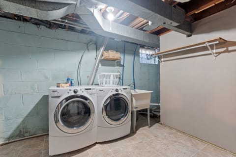 A well-organized basement laundry room with modern washer and dryer, utility sink, and storage space.