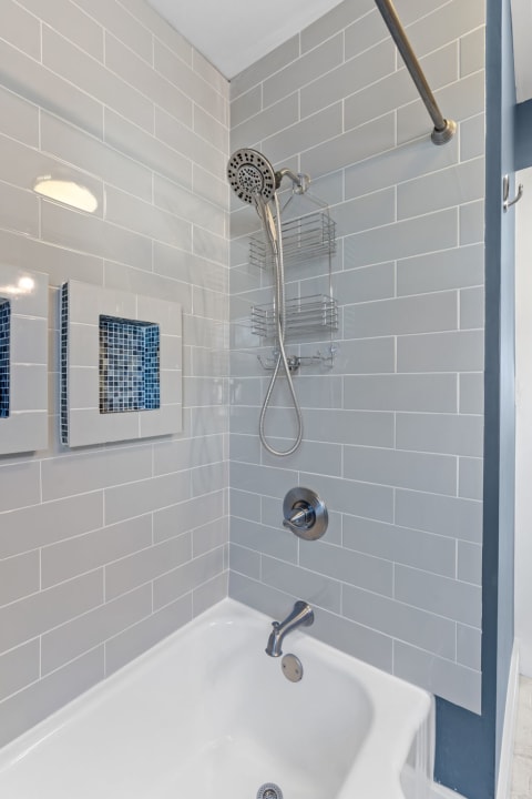 A view of a sleek tub-shower combination with gray subway tiles and shower accessories.