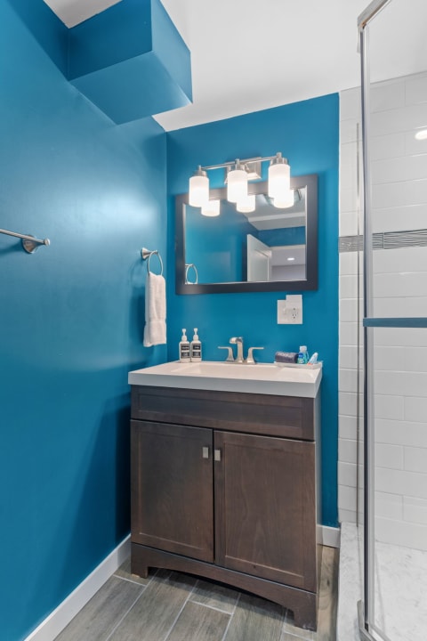 Vibrant bathroom featuring blue walls, a sleek vanity with a white countertop, and modern lighting fixtures.