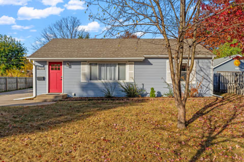 Gray house with a red door and autumn leaves in the front yard.