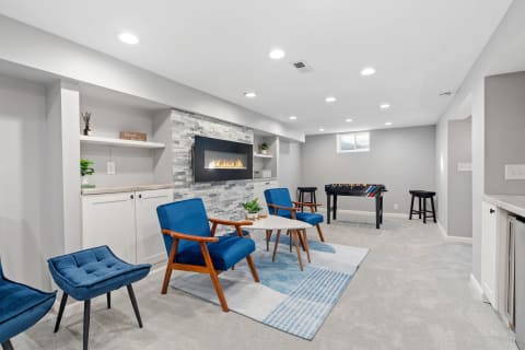 Stylish basement with blue chairs, electric fireplace, foosball table, and modern decor.