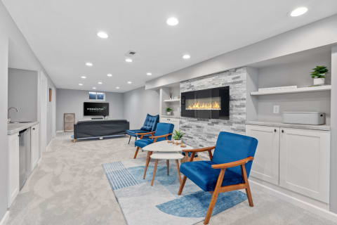 Stylish modern basement with blue chairs, a fireplace, and a kitchenette.