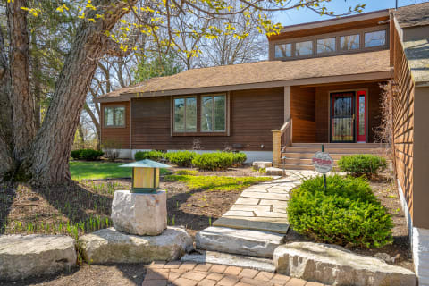 A rustic house with a red door and a stone pathway surrounded by greenery.