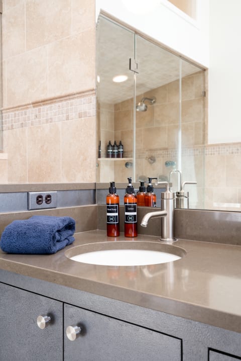 Stylish bathroom counter featuring a sink, hand soap, lotion, and navy towel.