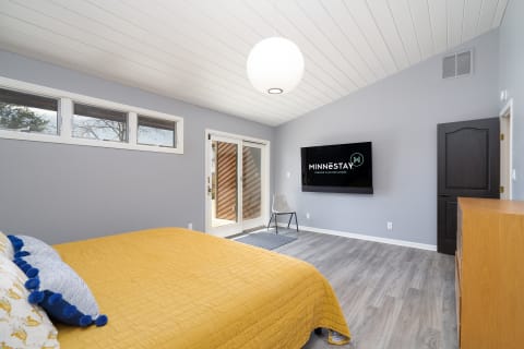 Contemporary bedroom with a queen-sized bed, minimalistic furniture, and a mounted TV.