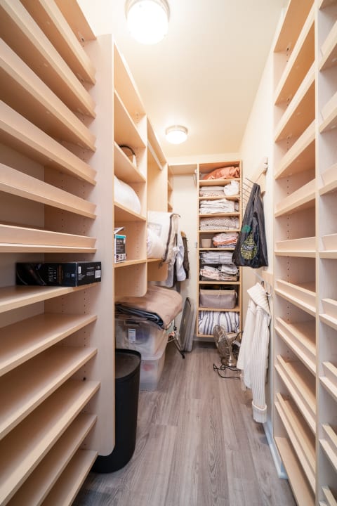 A narrow closet with light wooden shelves holding neatly arranged fabrics and blankets.