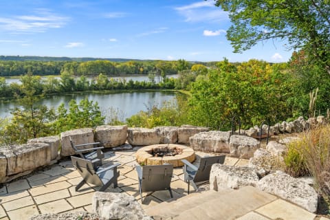 Outdoor fire pit area with lounge chairs overlooking a river and greenery.