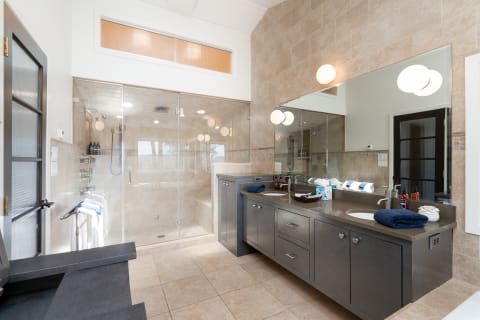 Spacious modern bathroom featuring a glass shower and dark vanity with natural light.