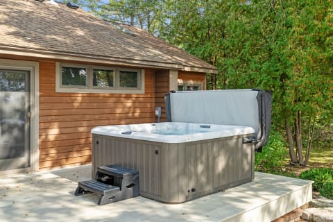 Hot tub on a wooden deck next to a house, with trees in the background.