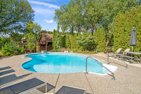 A swimming pool in a backyard setting with lounge chairs and a wooden house in the background.