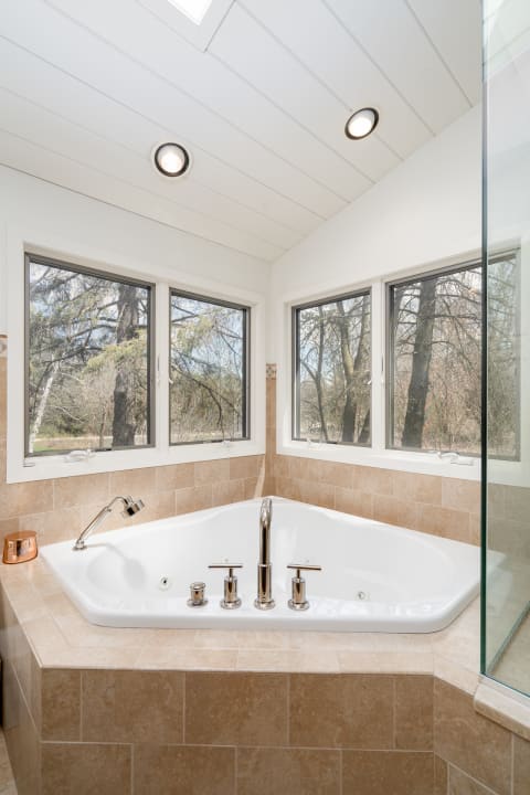 A corner jetted bathtub in a modern bathroom with large windows and natural light.
