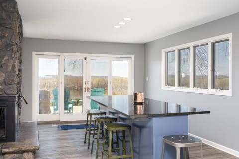 Interior view of a contemporary kitchen featuring an island, metal stools, and a fireplace with doors leading to a patio.